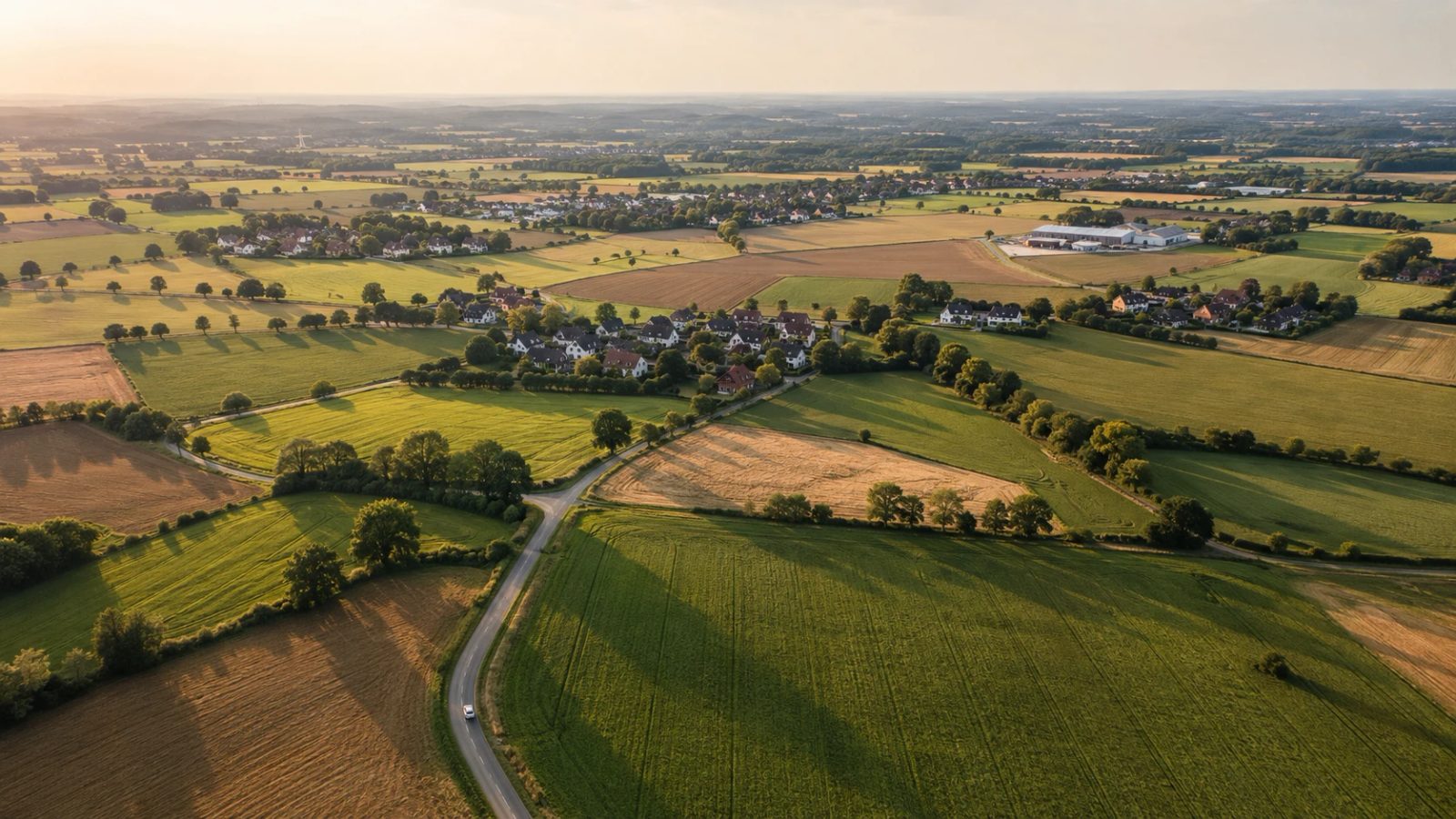 Luftaufnahme einer ostwestfälischen Landschaft im Abendlicht: Felder, Hecken und Landstraßen bilden natürliche Flächen, dazwischen Dörfer und ein Gewerbegebiet