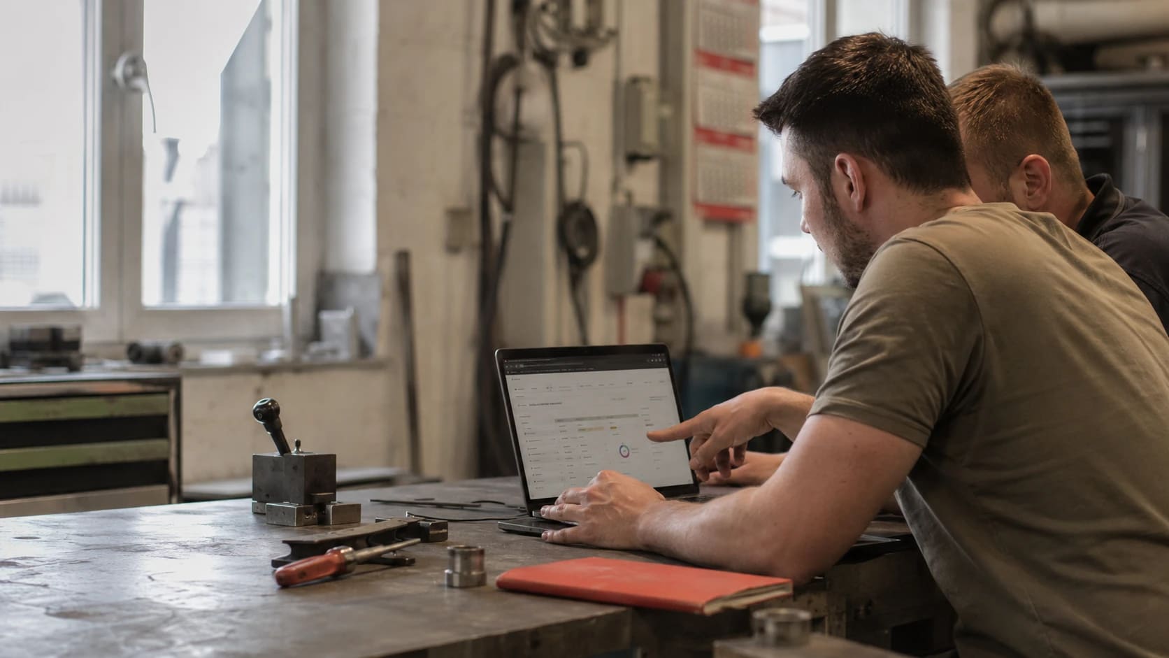 Symbolbild: zwei Personen stehen an einer Werkbank zwischen Werkzeug und schauen gemeinsam auf einen Laptop